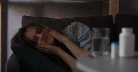 Young woman is lying on couch, suffering from headache and drinking water. Girl suffers from migraine.