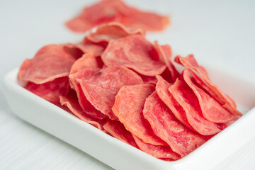Closeup view of salted slices of jerky pork or beef organic tasty meat dehydrated or dried  full of protein served as healthy snack or appetizer in plate on white wooden background. Horizontal