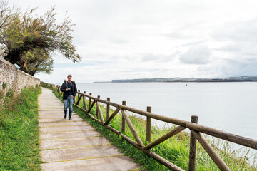 Young guy walking on promenade near sea on cloudy day