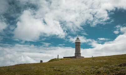 Lighthouse on grassy hill under cloudy sky