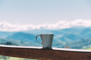 cup of coffee placed on wooden fence against amazing mountain landscape on sunny day