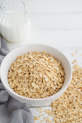 Raw dry oatmeal flakes in a bowl with milk on a white wooden background. Healthy food. Copy space.