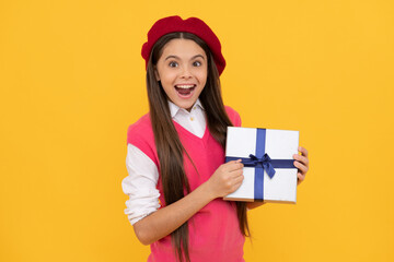 surprised teen girl in french beret hold present or gift box on yellow background, shopping