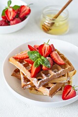 Fresh crisp Belgian waffles with ripe strawberries, mint and honey for breakfast on a light background.