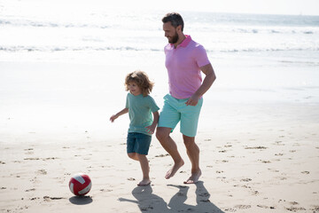 father and son play soccer or football on beach. daddy with kid boy on summer day.