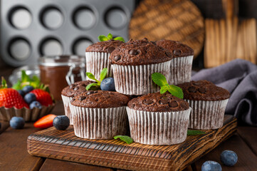 Chocolate muffins or cupcakes with chocolate drops on a dark wooden background with fresh berries and mint. Copy space.