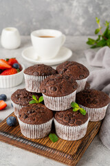 Chocolate muffins or cupcakes with chocolate drops on a wooden board on a gray background with fresh berries and mint. Copy space.