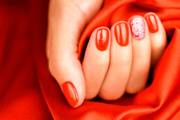 Female hand with a red manicure with a pattern. Beautiful manicure on a red silk background.
