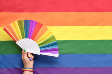 Hand with hand fan on rainbow LGBTQIA background, flat lay with text space. Simple, minimal LGBT...