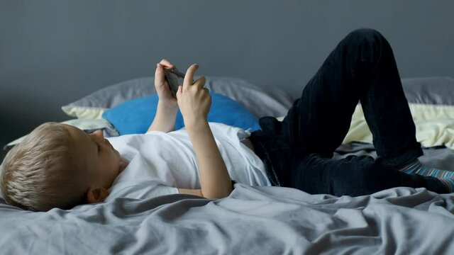 Child Playing A Game on A Smartphone, boy playing smartphone on bed, kid use phone and play game, addicted game and cartoon