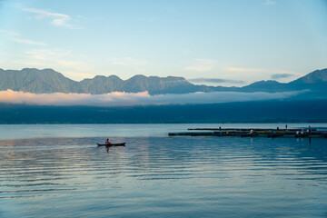 Fototapeta na wymiar Beautiful panoramic view of Lake Maninjau, West Sumatra, Indonesia in blue hour of the morning, with a small fishing boat sailing. Beautiful nature landscape of Indonesia.