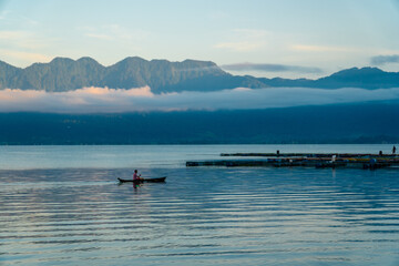 Beautiful panoramic view of Lake Maninjau, West Sumatra, Indonesia in blue hour of the morning, with a small fishing boat sailing. Beautiful nature landscape of Indonesia.