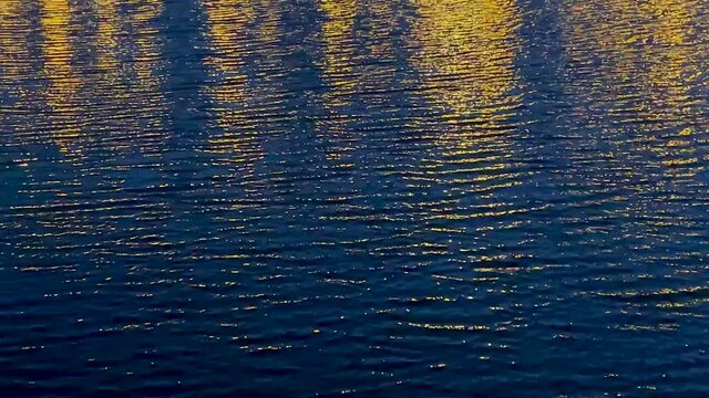 Beautiful glare from the lanterns on the lake in the park close-up. Video of iridescent highlights on the water for a 4K background.