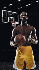 Portrait of young African sportsman, basketball player stading with ball in gym, idoors isolated on...