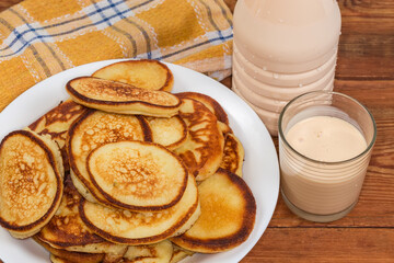 Freshly fried oladyi on dish, fermented milk on rustic table