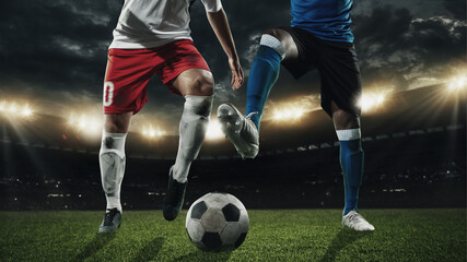 Two male soccer, football players dribbling ball at the stadium during sport match on dark sky...