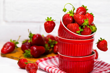 Juicy Fresh Strawberries in a Red Bowl on a piece of cloth on a white Brick background. Vitamin food. Copy space. Equilibrium floating food balance. Fruit Levitation.
