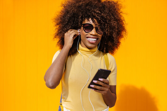 Happy black woman in earphones surfing internet on smartphone outdoors