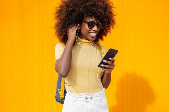 Happy black woman in earphones surfing internet on smartphone outdoors