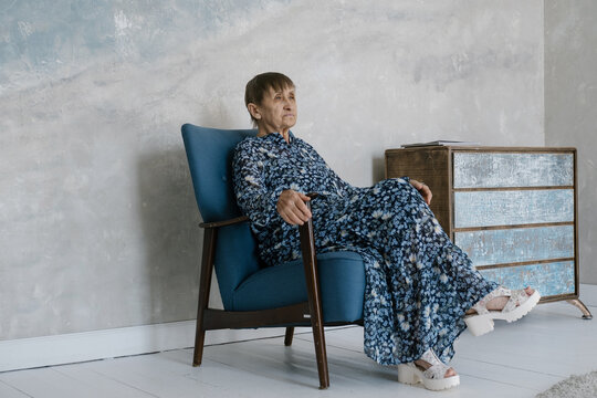 Beautiful elderly woman wearing dress sitting on armchair is thinking about something