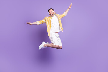 Fototapeta na wymiar Photo of pretty impressed mature man dressed yellow shirt glasses smiling jumping high isolated purple color background