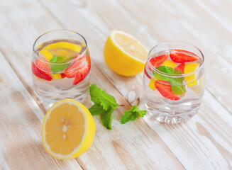two glasses of lemon, strawberry and mint drink and lemon halves on the table. homemade summer refreshing drink.