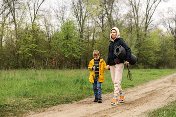 A mother and a young son walk in the park. A woman with a tourist mat and a boy walk about the road in the park, the forest.