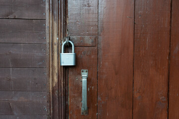 The brown wooden door of the village house is padlocked. Part of the wall is visible, sheathed with horizontal boards. Background. Texture.