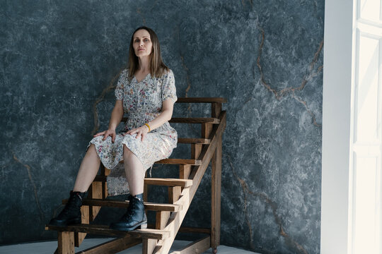 Home portrait of beautiful middle aged female sitting on wooden stairs