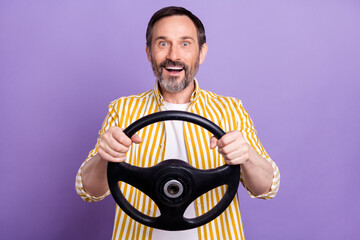 Photo of positive amazed happy mature man hold hands steering wheel isolated on purple color background