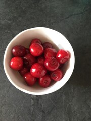 Red, burgundy sweet ripe cherries in a white plate on a black table background