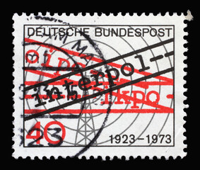 A stamp printed in Germany showing a transmission tower with radio waves and Interpol, 50th anniversary of International Criminal Police Organization, circa 1973