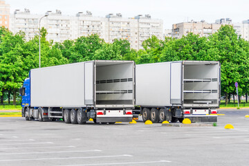 Two trucks in a parking lot with an empty container trailer open gates at the back, ready to load...