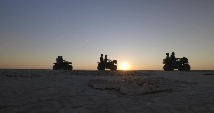 Silhouette view of tourists having fun riding quad bikes in the wide open spaces of the spectacular Makgadikgadi Pans at sunset,Botswana