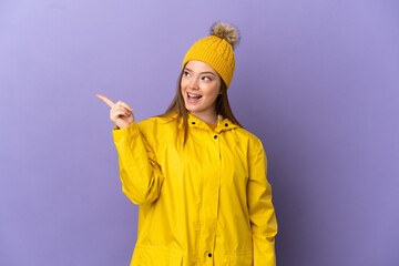 Teenager girl wearing a rainproof coat over isolated purple background intending to realizes the solution while lifting a finger up