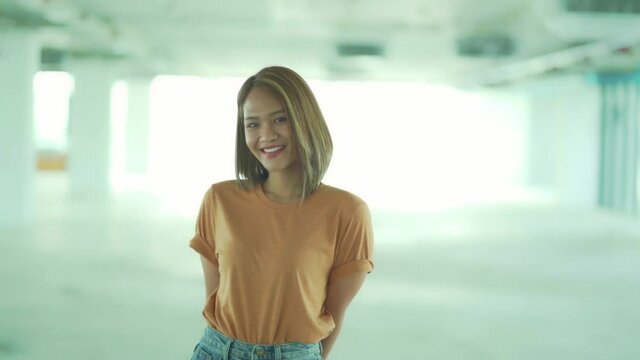 Stylish Asian girl wearing orange t-shirt and jean skirt posing in empty room, urban clothing style. Street photography.
