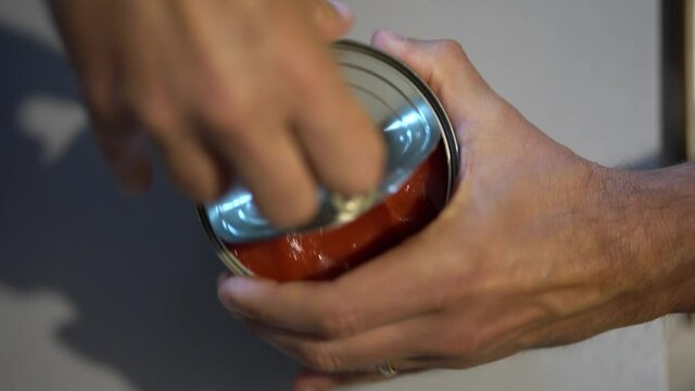 Un homme ouvre une conserve de tomates.