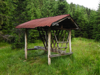 A wooden feeder built for storing hay having the purpose on providing food for wild deer. The building is located on an alpine pasture, near a coniferous forest.