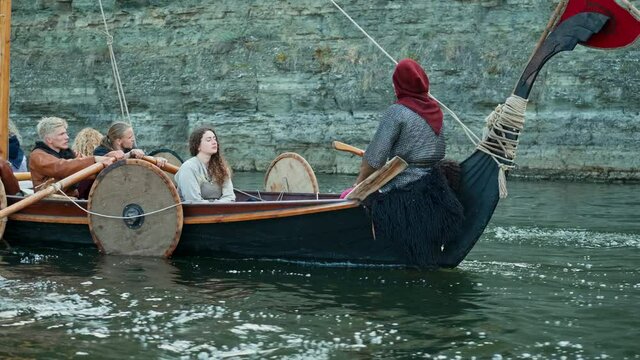 Vikings Sail on an Old Ship Along a Quiet River Against the Backdrop of a Rocky Coast. The Men Row the Oars Diligently Towards Adventure. Medieval Reconstruction.