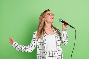 Photo of cheerful young joyful woman enjoy sing karaoke microphone wear glasses isolated on green...