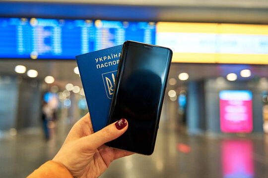 Passport And Phone In Hand On The Background Of The Airport Information Board. Travel With The Minimum Amount Of Stuff