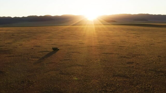 Spectacular epic aerial view of a safari vehicle driving into the sunset through the grassy vegetation famous fairy circles in the Namib desert 