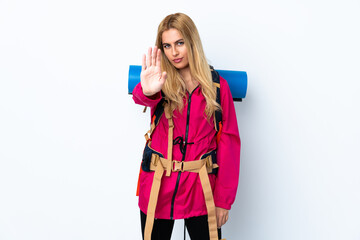 Young mountaineer woman with a big backpack over isolated white background making stop gesture with her hand