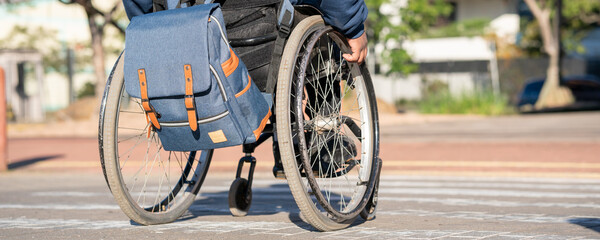sunny day and person in wheelchair with blue backpack crossing the street.