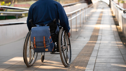 detail of backpack in wheelchair ascending ramp to train station.