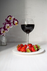 Red strawberries on plate with wine glass on white background and orchid flower in vase