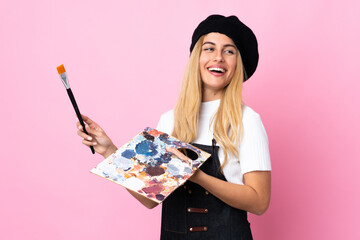 Young artist woman holding a palette over isolated pink background