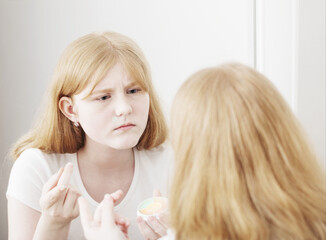 teen girl examines acne in front of mirror
