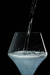 Mineral water is poured into a glass. Black background.