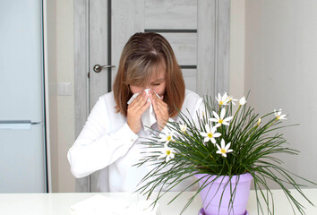 Young woman with allergies, holding face cloth and sneezing, flowers in the foreground. A girl...